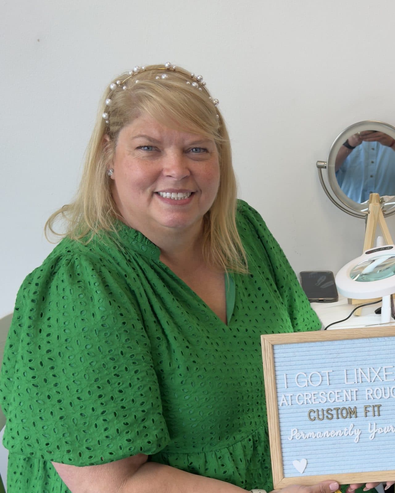 Tracey smiling in a green dress at her permanent jewelry table